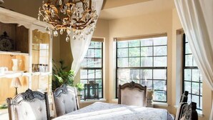 Una habitación con cama, candelabro y ventanas amplias.