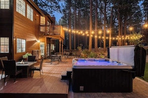 Et træhus med jacuzzi, udendørs møbler og lyskæder.