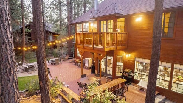 Una cabaña de madera con terraza, asientos exteriores y un gran ventanal con vistas al bosque.