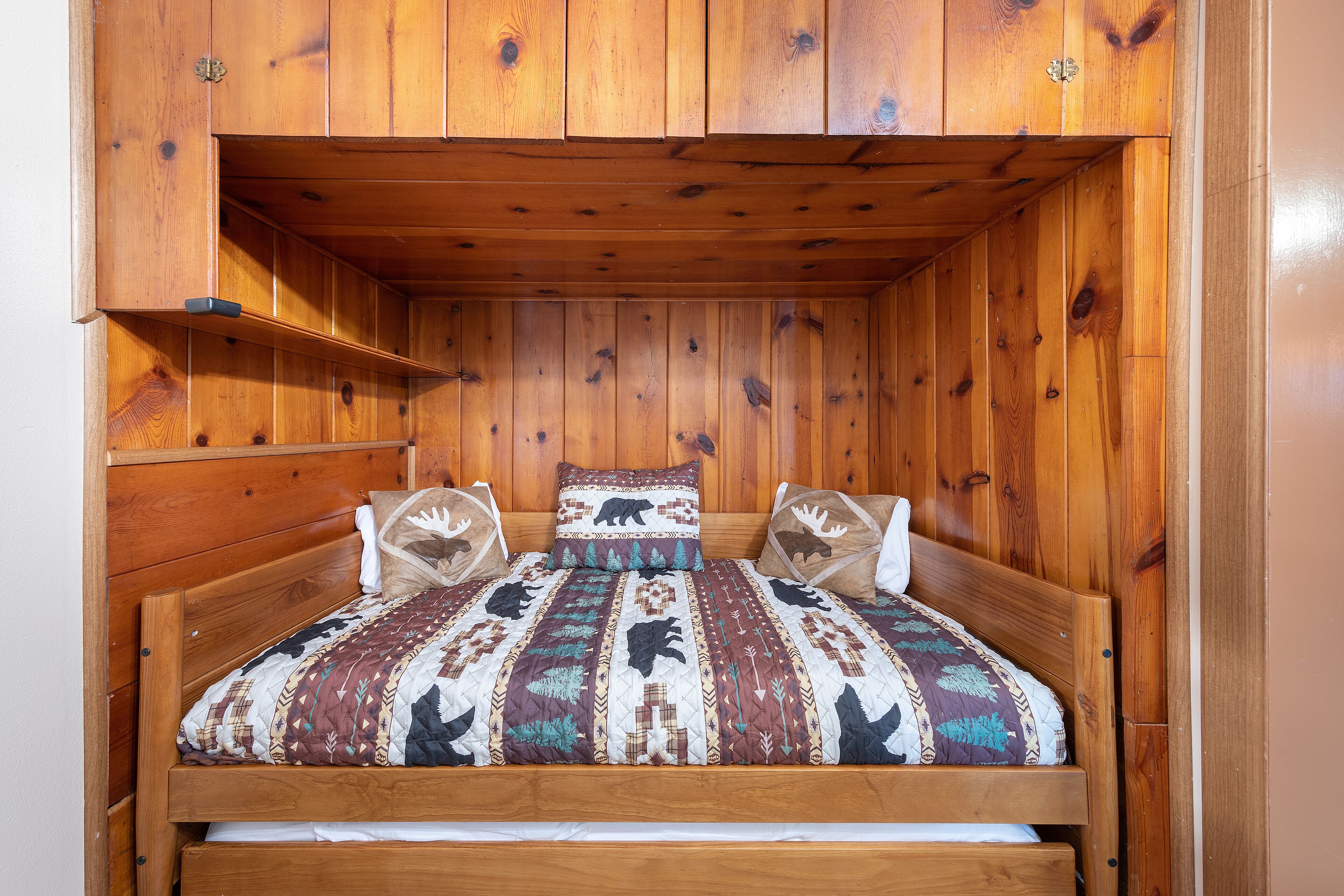 Un lit superposé en bois, avec une couvre-lit à motifs et deux oreillers décorés d’animaux.