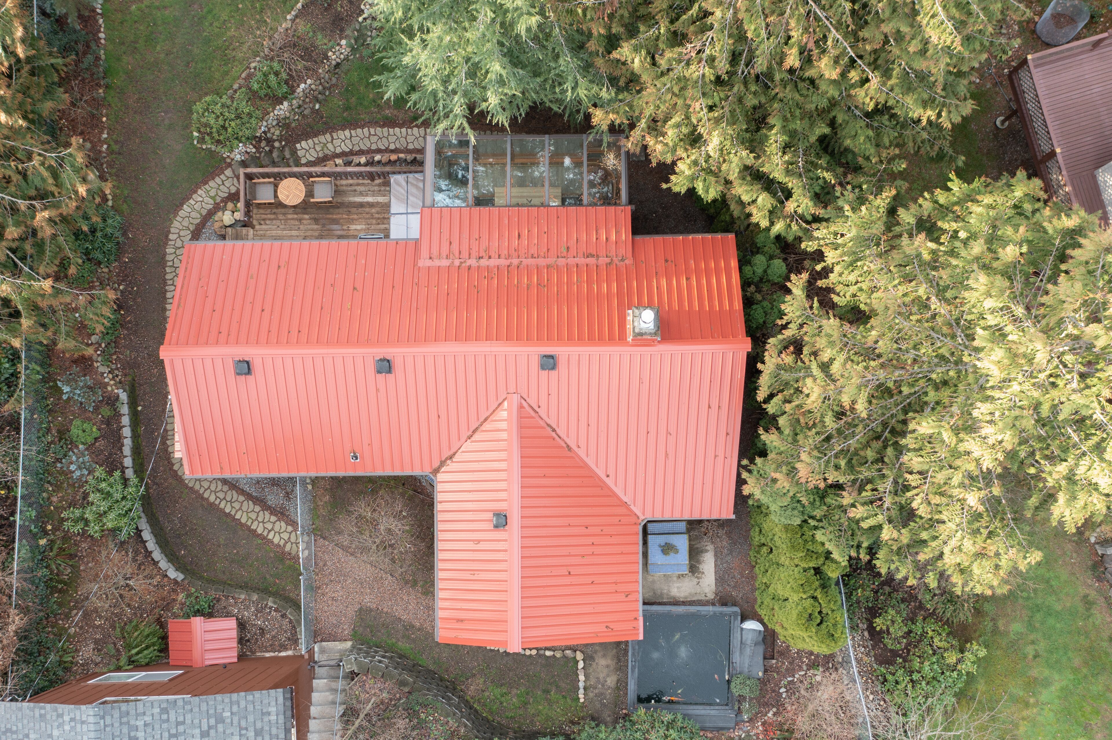 Un edificio con tetto rosso e un'ampia terrazza, circondato da alberi e un vialetto in pietra.