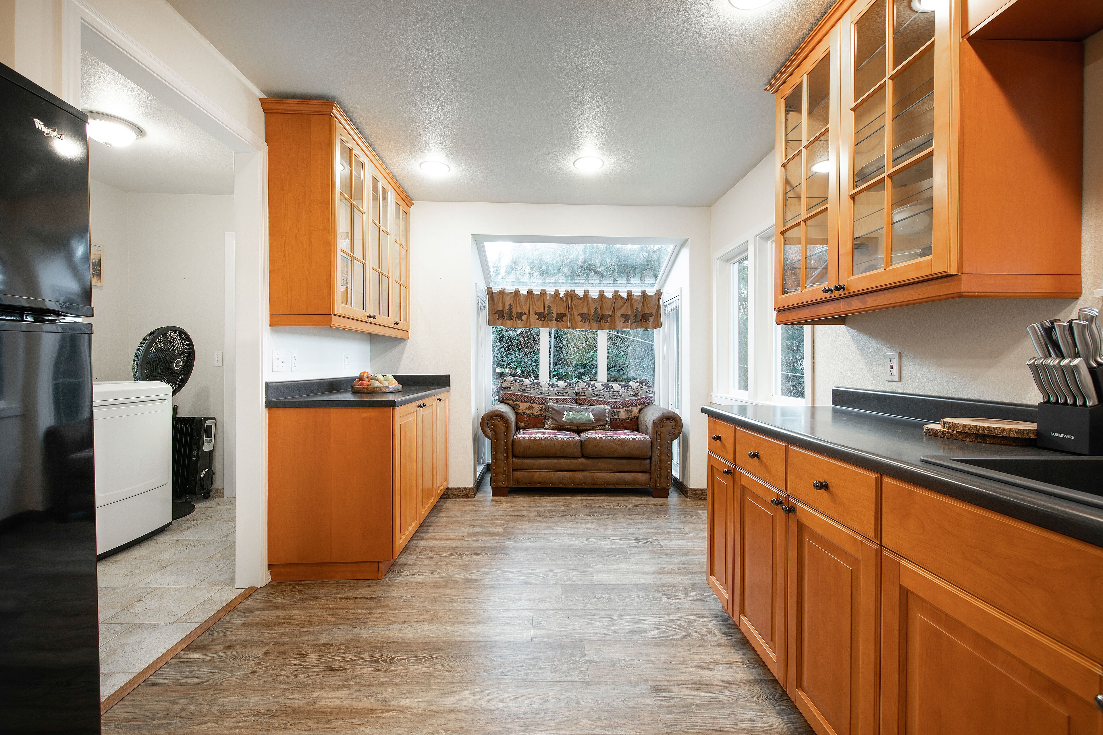 A kitchen with wooden cabinets, a black countertop, and a window with a view of trees.
