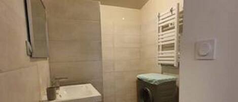 A small bathroom with a sink, mirror, and a washing machine.