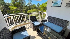 A covered outdoor seating area with wicker furniture and a glass table, overlooking a natural landscape. - Holiday apartment modern with balcony (Jadranovo)