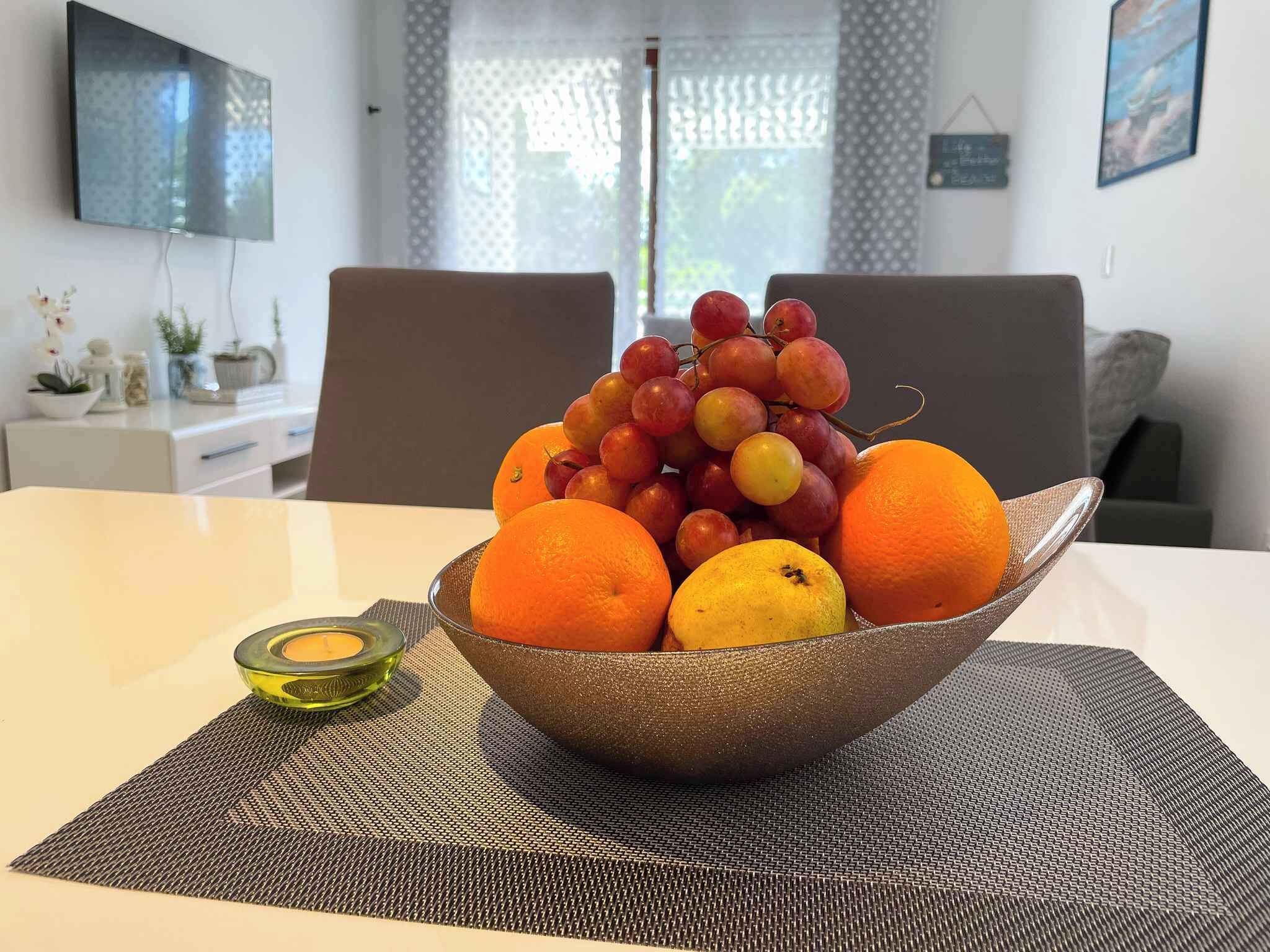A dining table with a bowl of fruit, a candle, and a placemat.