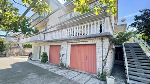 Un edificio de dos pisos con un balcón, una puerta de garaje roja y una escalera que lleva a un nivel superior.