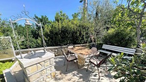 Un patio al aire libre con una zona de barbacoa de piedra, una mesa de madera y sillas.