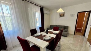A dining area with a table set for four, a sofa, and a door leading to another room. - Holiday apartment with balcony and air conditioning (Jadranovo)