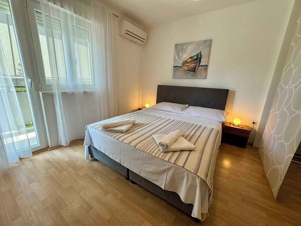 Una cama bien hecha con ropa de cama a rayas y almohadas, un cuadro sobre ella, y un piso de madera.