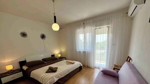 A bedroom with a bed, bedside tables, a sofa, and a window with curtains. - Holiday apartment with balcony and air conditioning (Jadranovo)