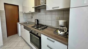 A modern kitchen with white cabinets, a stainless steel stove, and a coffee maker. - Holiday apartment with balcony and air conditioning (Jadranovo)