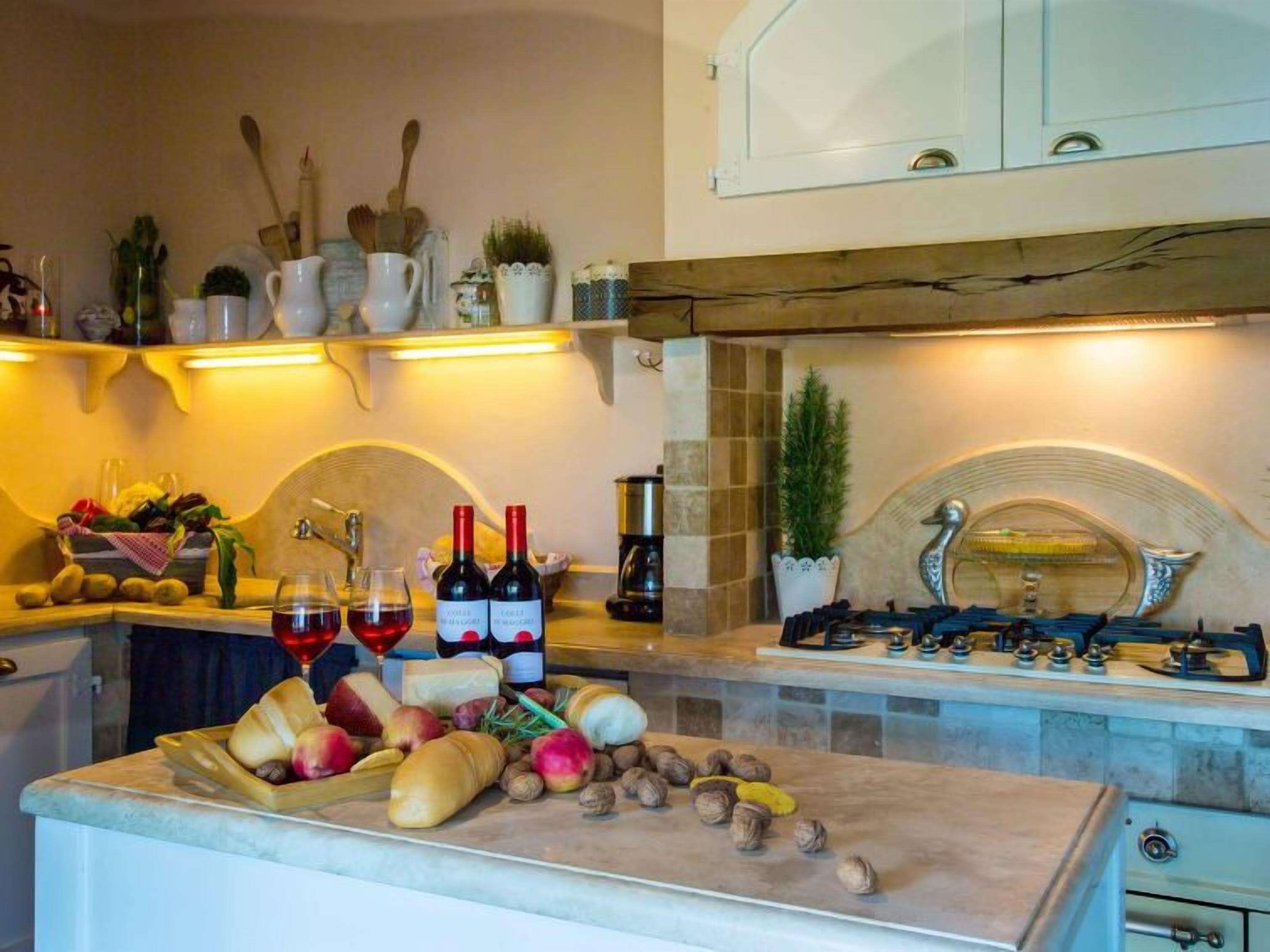 A kitchen with a marble countertop, a gas stove, and various kitchen utensils. There are two bottles of wine, a bowl of fruits, and a potted plant on the counter.