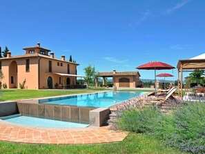 A large house with a swimming pool, outdoor seating, and a clear blue sky.