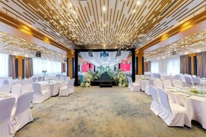A conference room with round tables and chairs, a stage with floral decorations, and a modern ceiling design. - General Hotel (Longquan)