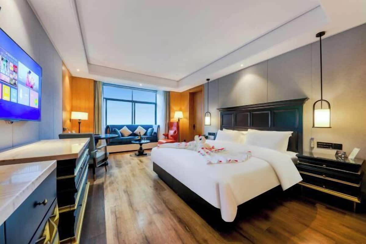 A modern hotel room with a large bed, a desk, a sofa, and a TV.