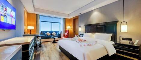 A modern hotel room with a large bed, a desk, a sofa, and a TV.