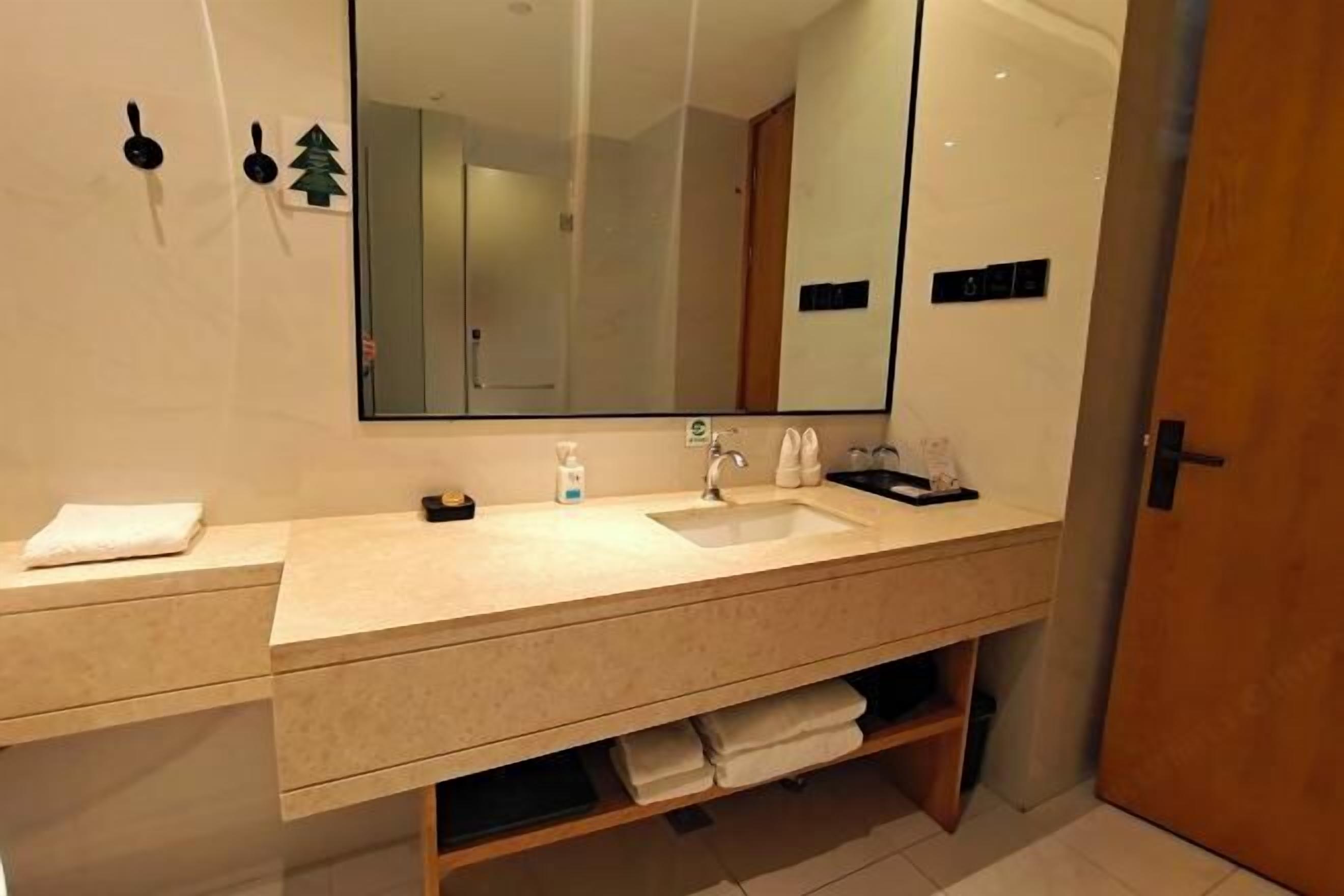 Een moderne badkamer met een grote spiegel, een wastafel en een opbergmeubel. Handdoeken en toiletartikelen liggen op het aanrecht.