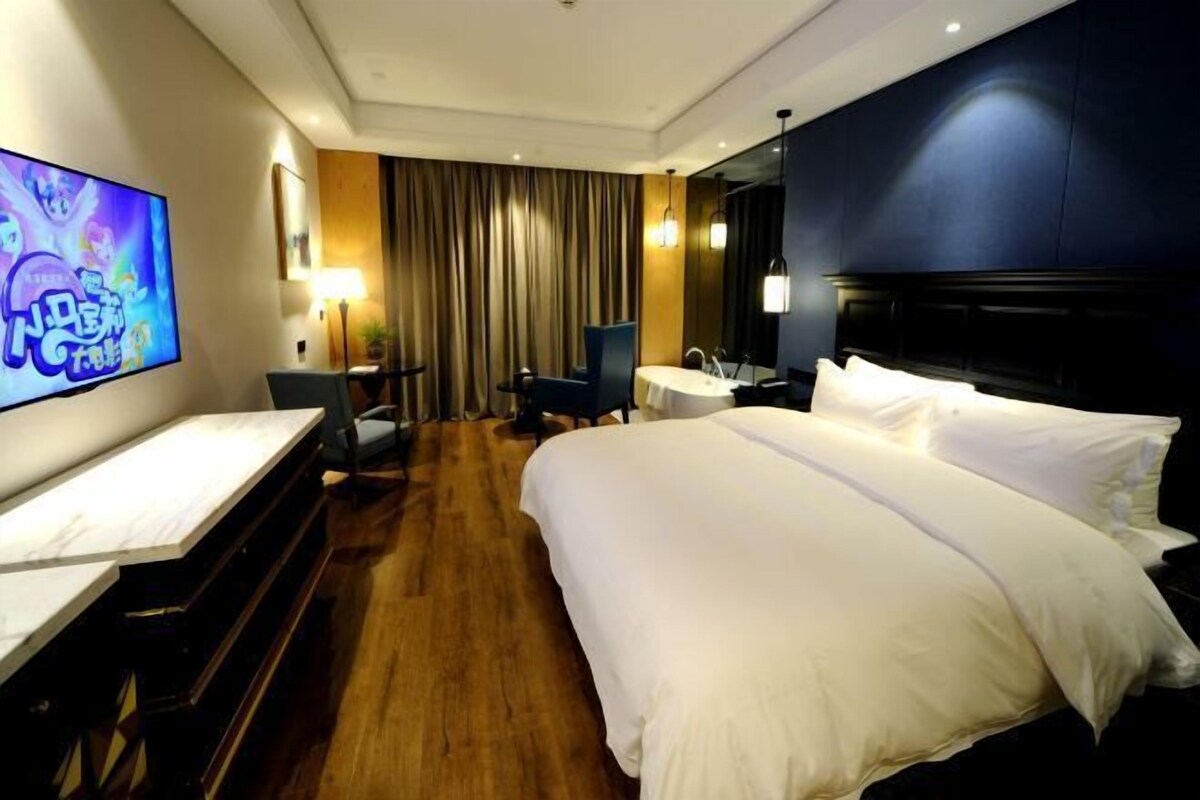 A hotel room with a large bed, a desk, a chair, a TV, and a table.