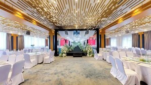 Un salón de conferencias con sillas y mesas blancas, un escenario con decoraciones florales y un techo con diseños lineales.