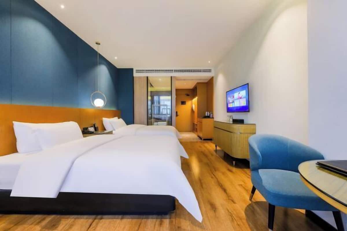 A modern hotel room with a large bed, a desk, a chair, and a television.