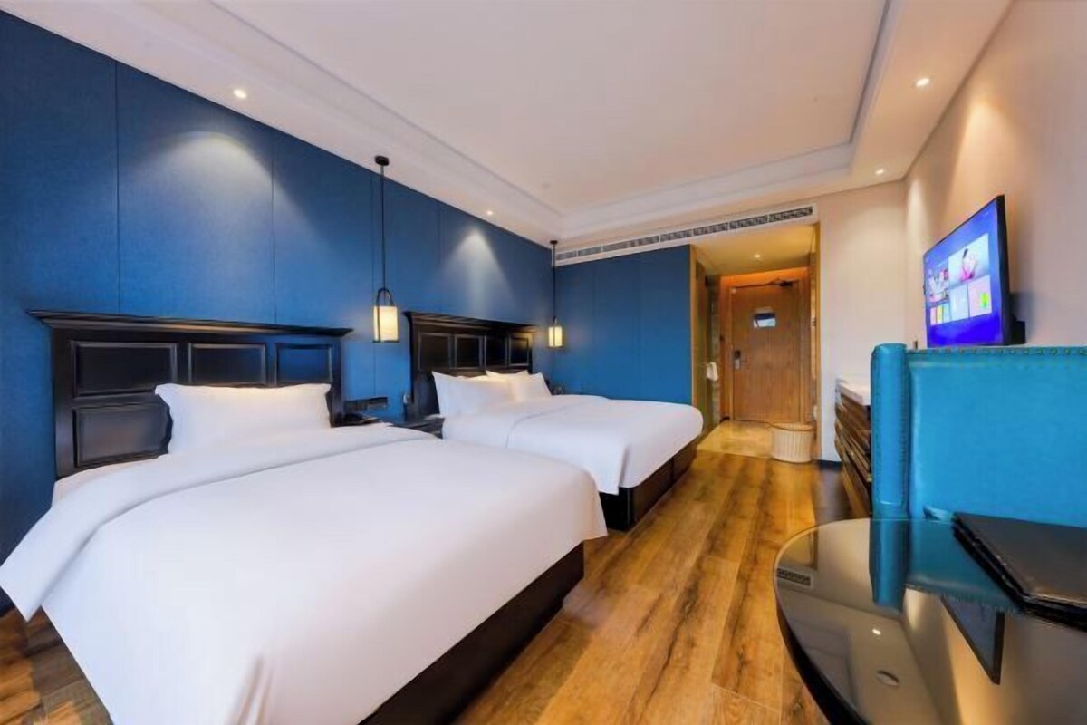 A hotel room with two beds, a TV, and a wooden floor.