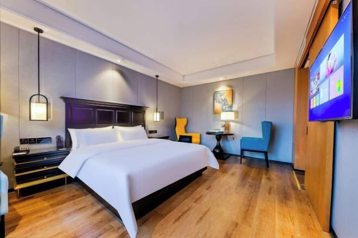 A hotel room with a large bed, a desk, a chair, a TV, and a painting on the wall.