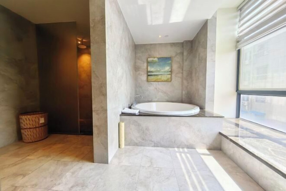A modern bathroom with a freestanding bathtub, a large window, and a painting on the wall.