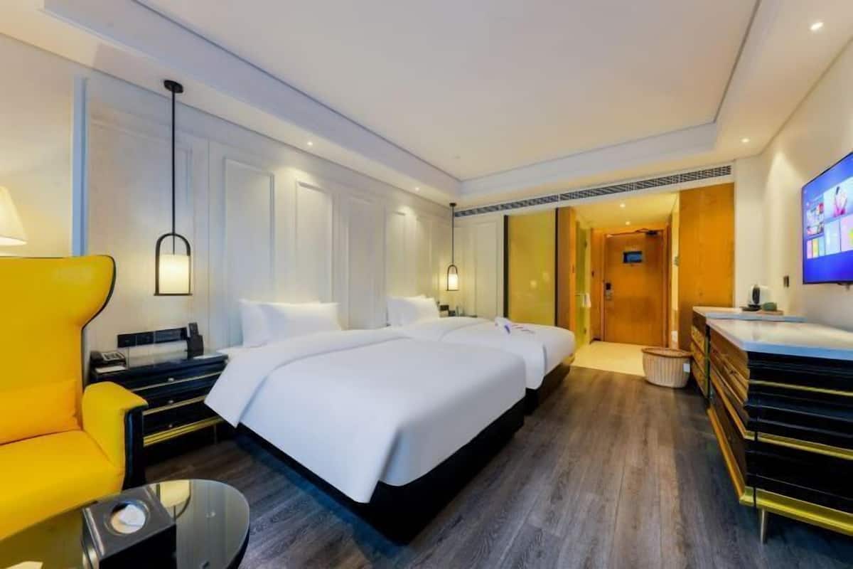 A hotel room with a large bed, a yellow armchair, a desk, and a television.