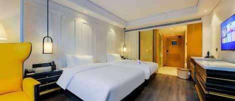 A hotel room with a large bed, a yellow armchair, a desk, and a television.
