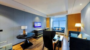 Una habitación de hotel moderna con una televisión de pantalla plana, una mesa de comedor, un sofá y una lámpara.