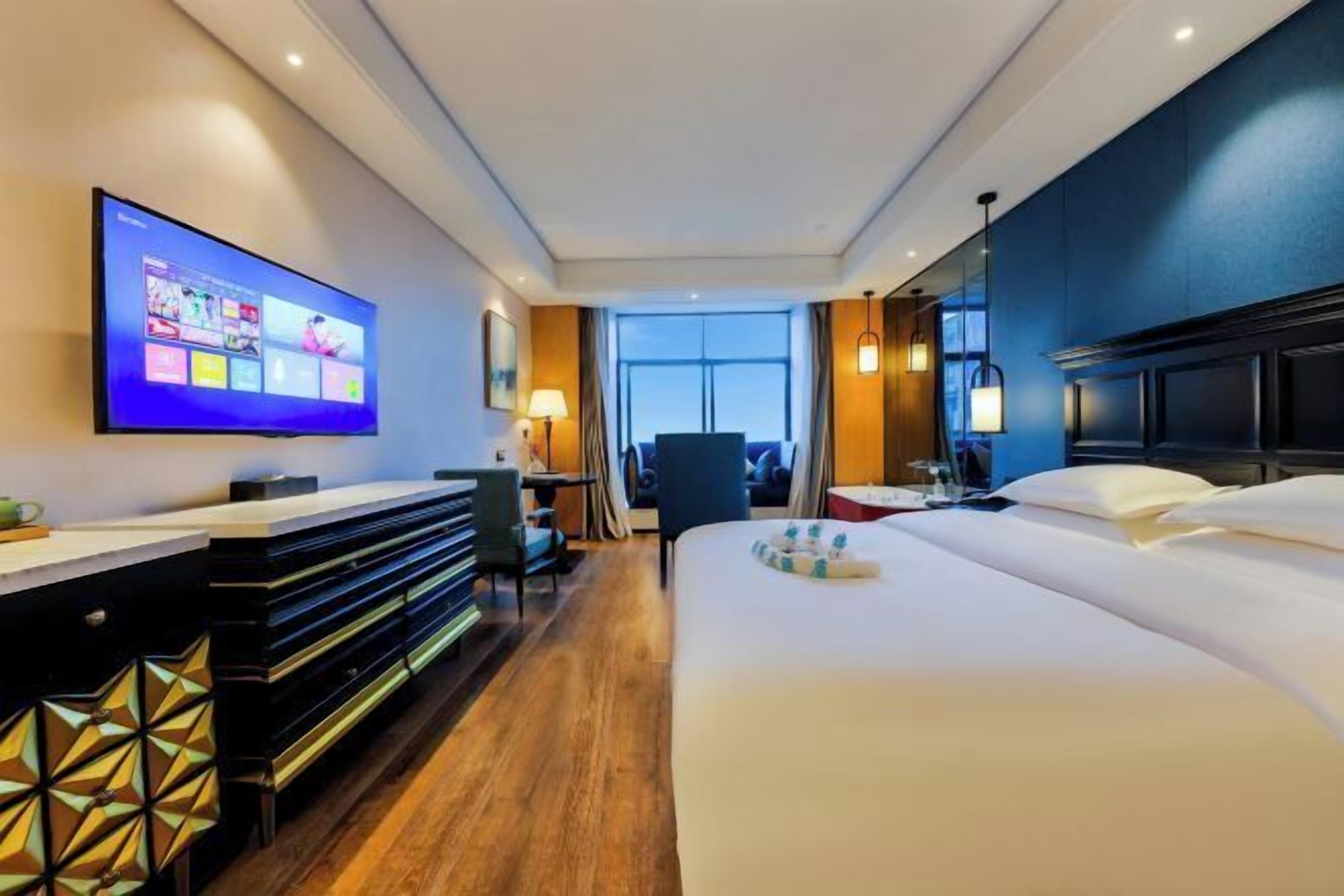 A hotel room with a bed, a desk, a TV, and a view of the outside.