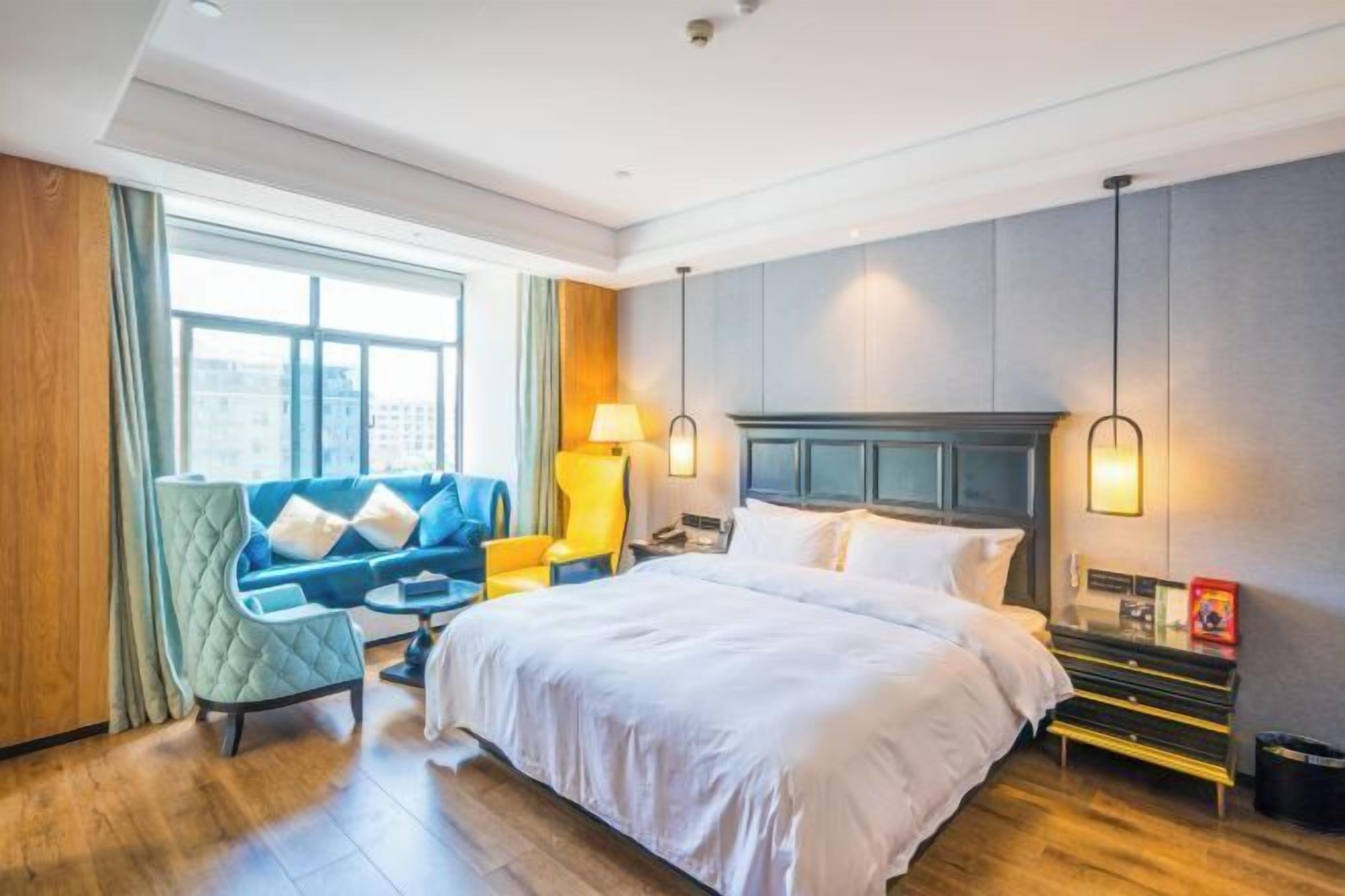 A hotel room with a large bed, a blue sofa, a yellow armchair, and a wooden floor.