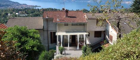 A two-story house with a red-tiled roof, a covered patio, and a view of a lake and mountains.