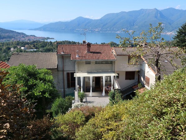 A two-story house with a red-tiled roof, a covered patio, and a view of a lake and mountains.