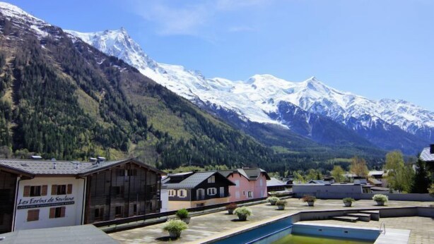 Una località montana con piscina, chalet in legno e cime innevate sullo sfondo.