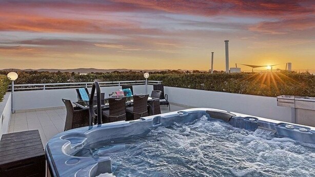 En tagterrasse med jacuzzi, udendørs møbler og udsigt til solnedgang.
