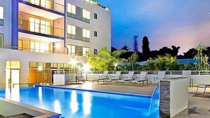 Et moderne hotel med swimmingpool, flere balkoner og udendørs siddepladser.