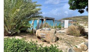 A beachside resort with a large palm tree, a rock with 'Massage' and 'Sleep' signs, and a small structure with a blue roof. - Villa Crystal Clear - Luxury Villa with Private Pool (Sint Maarten)
