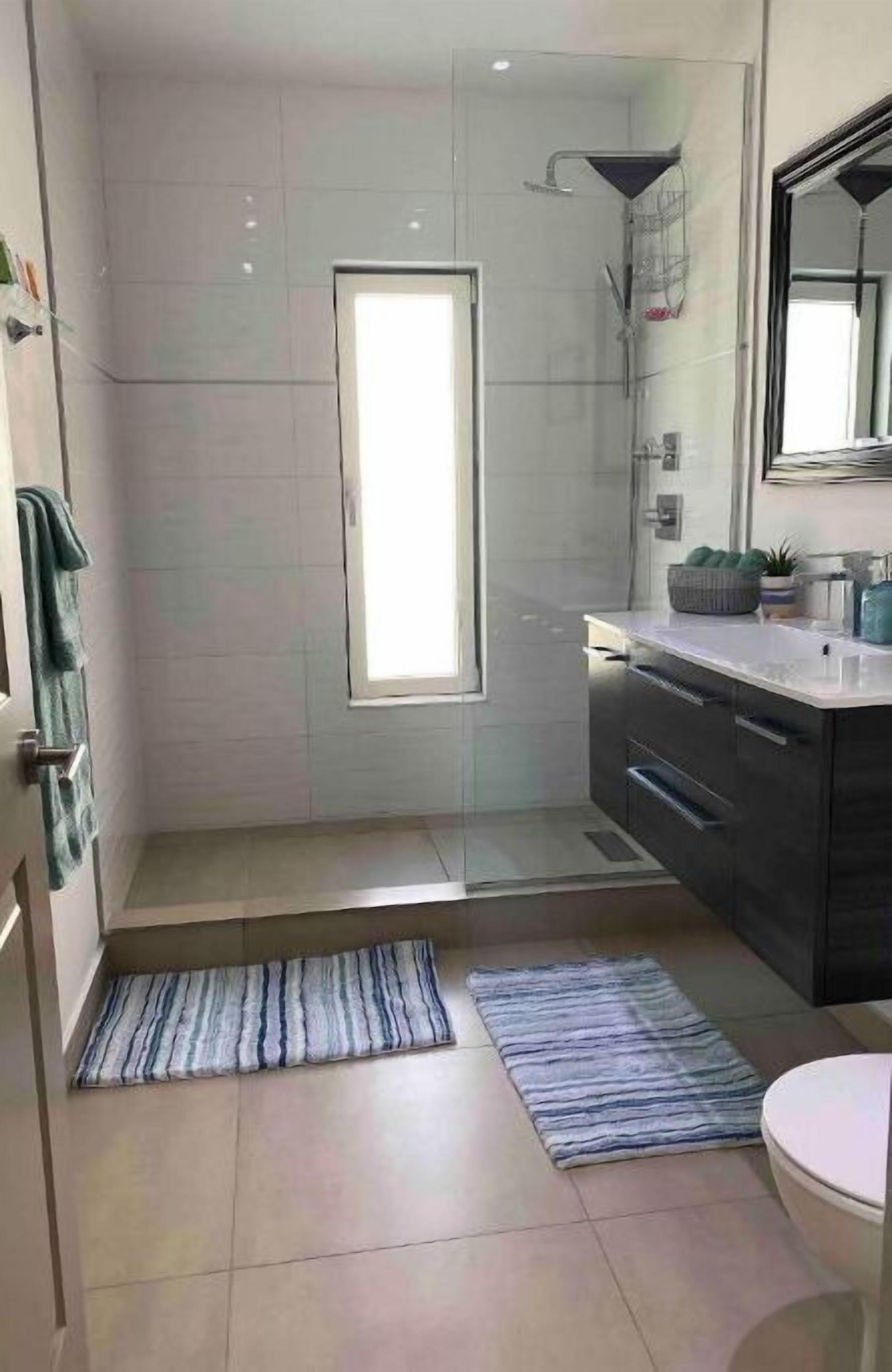 A modern bathroom with a glass shower enclosure, a large mirror, and a vanity with a sink and countertop.