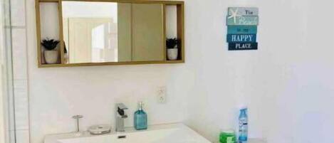 Un baño moderno con tocador de madera, un espejo grande, un inodoro y una pequeña estantería con plantas.