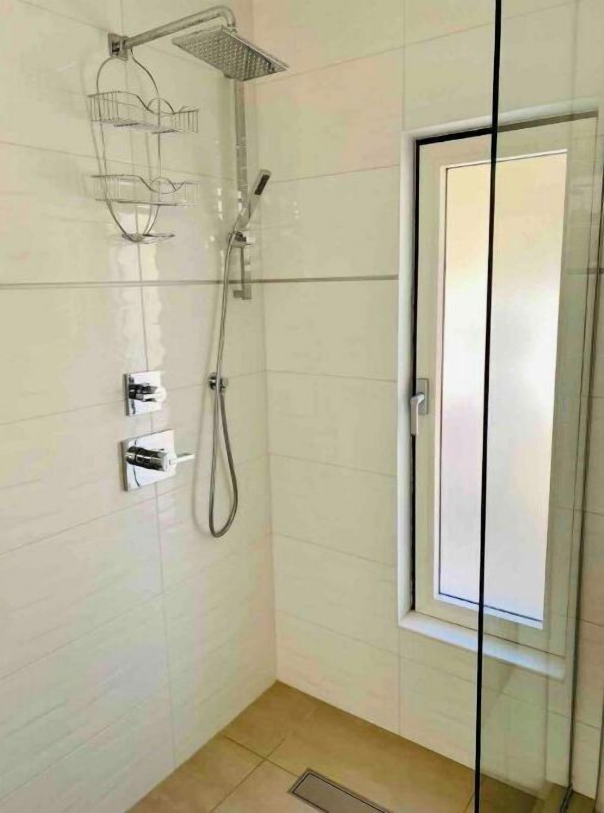 Une douche dotée d’une porte en verre, d’un pommeau de douche à main et d’un panneau de commande fixé au mur.
