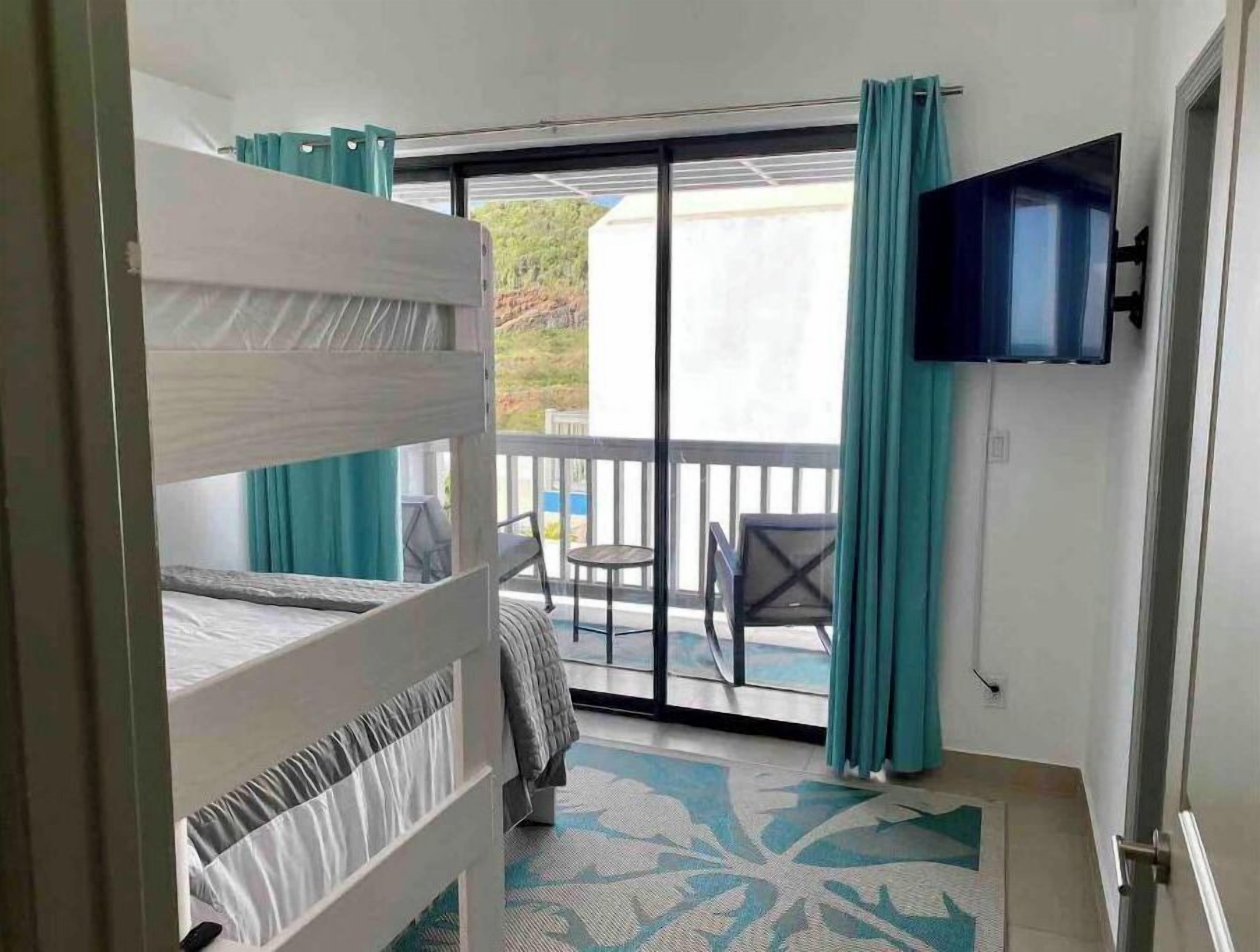 Habitación de hotel con literas, un balcón con mesa y sillas, y un televisor montado en la pared.