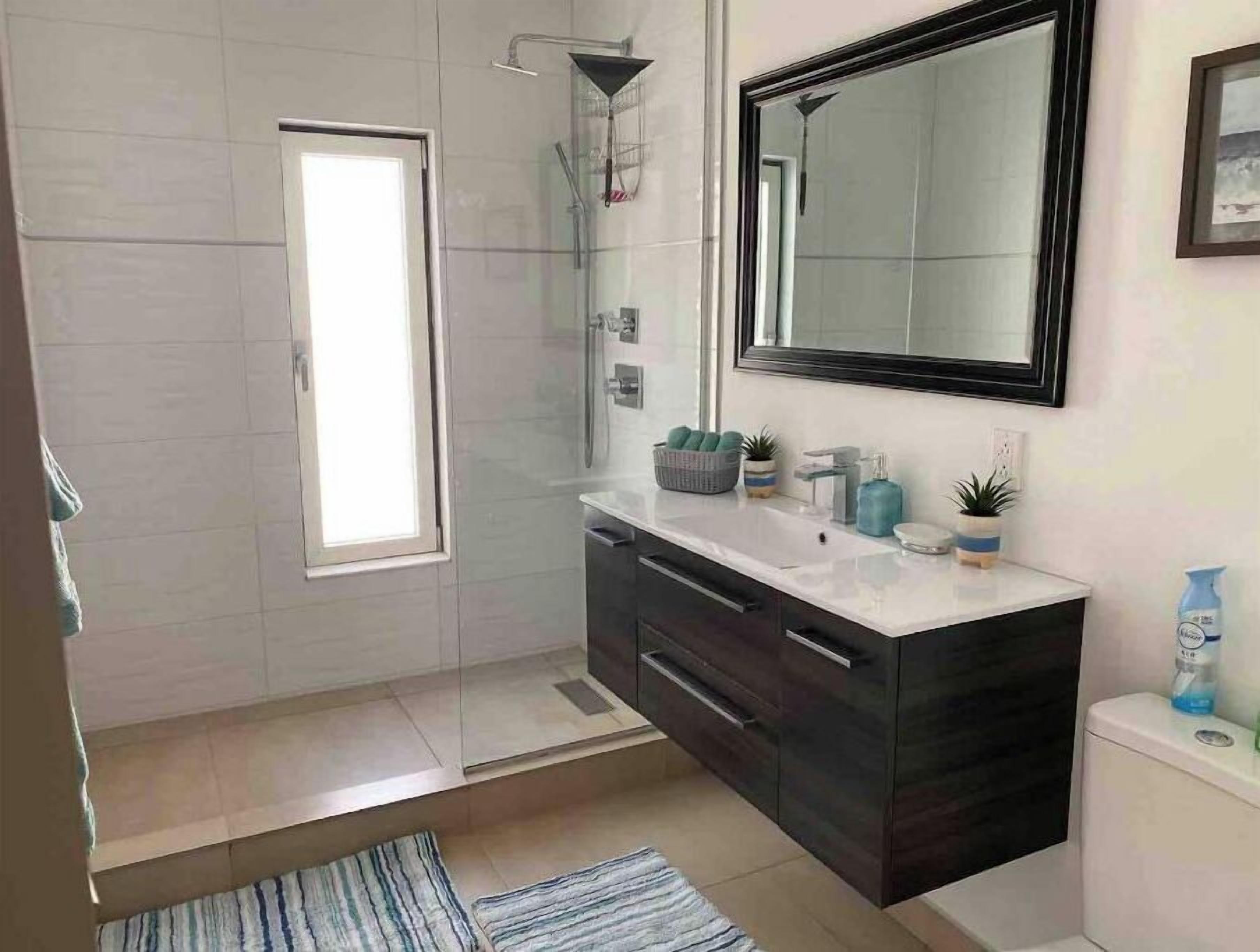 A modern bathroom with a glass shower enclosure, a large mirror, and a dark vanity with a white countertop.