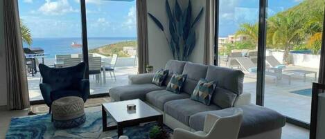 A modern living room with a large sofa, a coffee table, and a view of the sea.