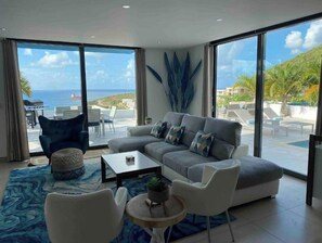 Enjoy the breathtaking view of the sea and mountains from this stylish living room with a comfortable sofa, coffee table, and armchair.