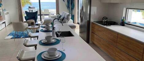 A modern kitchen with a large island, a dining area with a view of the ocean, and a kitchen counter with a sink and appliances.