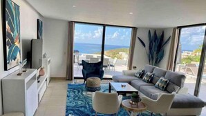 A modern living room with a grey sofa, a coffee table, and two chairs. There is a large window with a view of the sea. - Villa Crystal Clear - Luxury Villa with Private Pool (Sint Maarten)