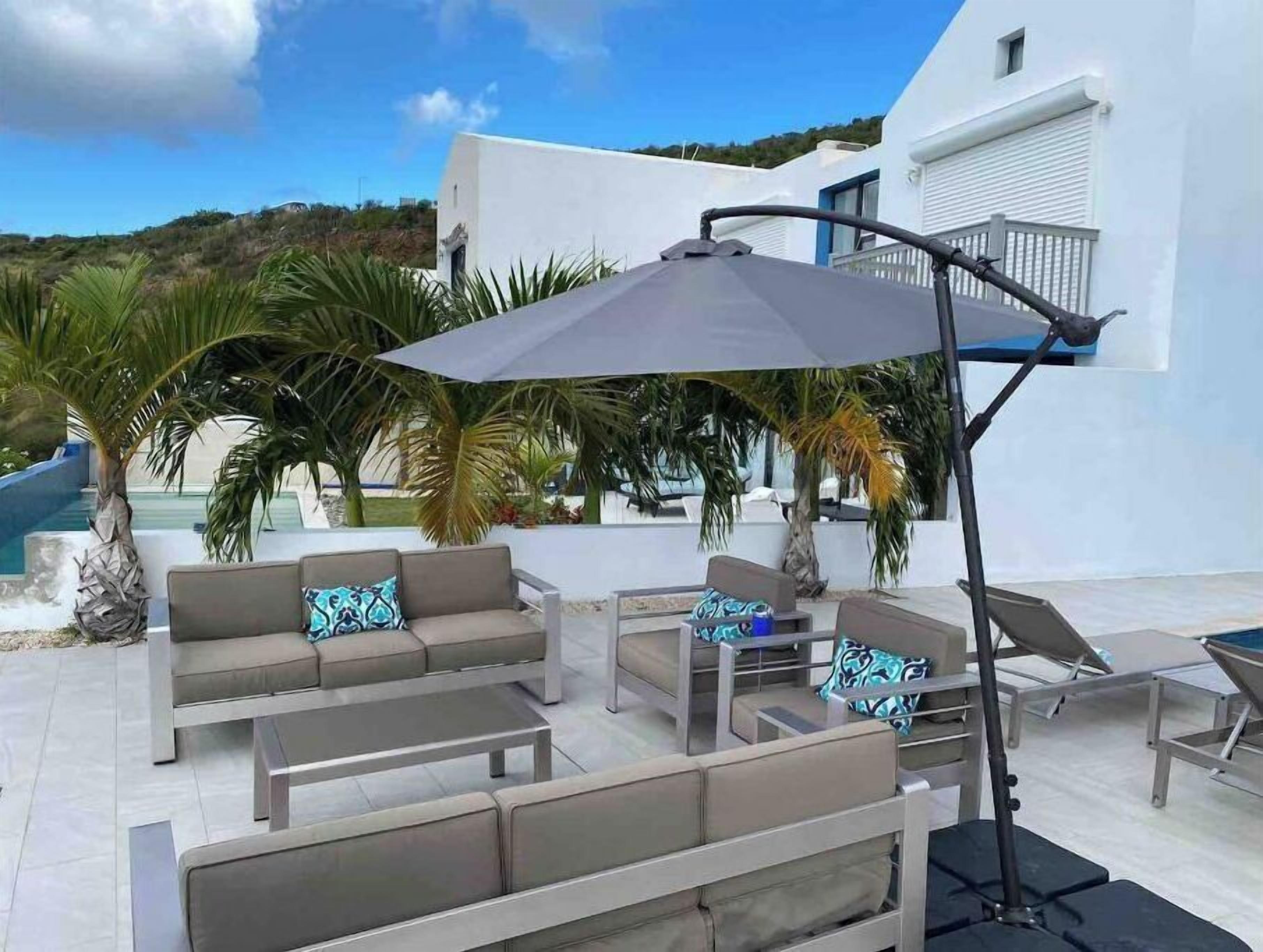 Een terras met een bank en stoelen, een tafel en een grote parasol.