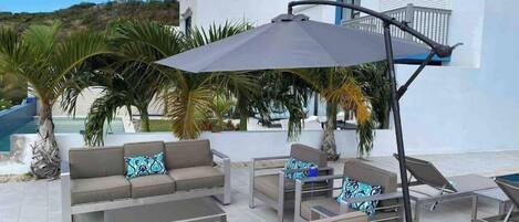 Een terras met een bank en stoelen, een tafel en een grote parasol.