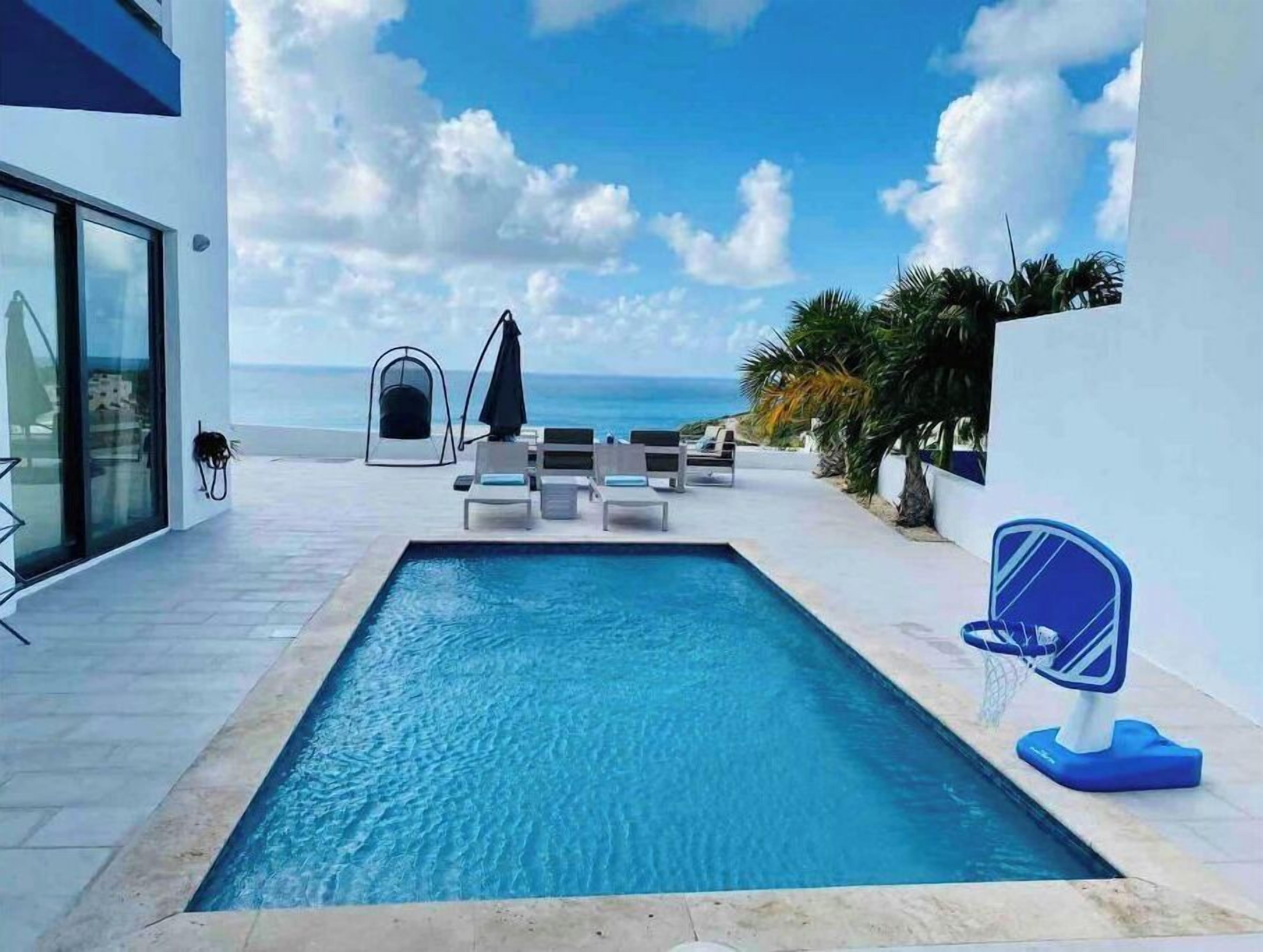 Ein Poolbereich mit Blick auf den Ozean, Liegestühle und ein kleiner Garten.